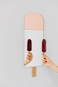 two hands holding popsicles in front of a mirror