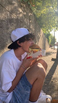 a man sitting on the ground eating a hot dog