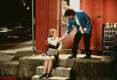 a woman sitting on the steps with a man standing next to her and holding hands