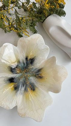 a white flower sitting on top of a table next to a vase with yellow flowers