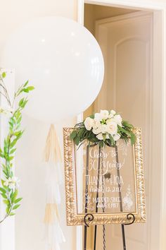 a sign that is on top of a stand with flowers and balloons in the background