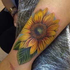 a sunflower tattoo on the arm with green leaves and yellow flowers in it's center