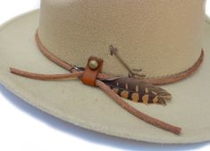 "The Victorio hat part of the Tucson Collection Type: Center Dent Western Wide Brim Fedora Adjustable Size: With a tie of a knot, adjust the fit of your hat to the ideal size from 21 ¼ to 23 ¼ inches. Dimensions: Wired Brim: 2 7/8\", Crown: 4\" Color: Distressed Camel, Sun bleached for 32 hrs. Materials: 65% Cotton , 35% Polyester Natural Leather Cord Leather Strap Ring neck Feather Handstitched Arrow & Horse motif Origin: All of our hats begin in Ecuador as the body is molded, then complete Custom Adjustable Fedora For Outdoor, Artisan Adjustable Fedora For Outdoor, Adjustable Handmade Leather Hat Bands, Adjustable Western Fedora For Hunting, Adjustable Fedora Hat Bands For Hunting, Handmade Adjustable Fedora For Outdoor, Adjustable Western Hat Bands For Hunting, Adjustable Country Style Fedora For Hunting, Adjustable Western Hunting Hats