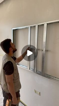 a man standing in front of a window with tools on his hand and looking at it