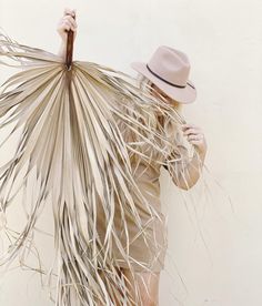 a woman in a straw hat and dress holding a large palm fronde over her head