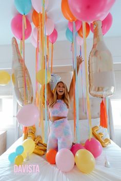 a woman standing on top of a bed surrounded by balloons