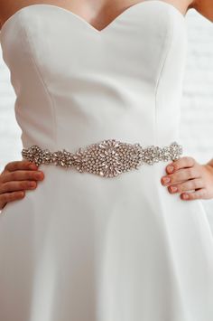 a woman wearing a white wedding dress with a crystal belt