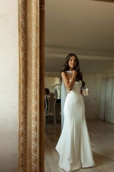 a woman standing in front of a mirror wearing a white dress and holding a cup