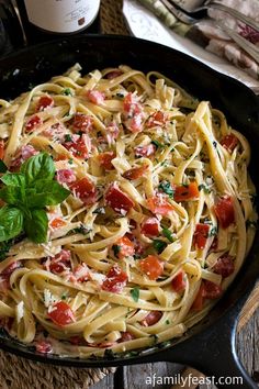 a skillet filled with pasta, tomatoes and parmesan on top of a wooden table