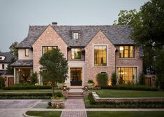 a large brick house with lots of windows and landscaping around the front door, surrounded by greenery