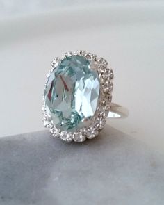 "✤ I can make this ring with many other colors. Please just contact me. ✤ MATCHING JEWELRY HERE: https://etsy.me/3dyGpV6 https://etsy.me/3pRn9ot https://etsy.me/3pGuKWv ✤ Size approx - The oval shape is approx. 19 mm x 15 mm ✤ Ring size: Adjustable. Elegant Thin adjustable band. ✤ Available also other metal finishes. Just choose at \"Metal type\" box. ✤ Colors: aquamarine, clear crystals. silver finish. ✤ Stones are hand set in secure prongs. ✤ One year warranty ✤ Nickel Free ✤ Bridal - Bridesma Oval Aquamarine Ring, Aquamarine Cocktail Ring, Teal Necklace, White Opal Earrings, Blue Pendant Necklace, March Birthstone Ring, Crystal Cuff Bracelet, Teal Earrings, Swarovski Ring