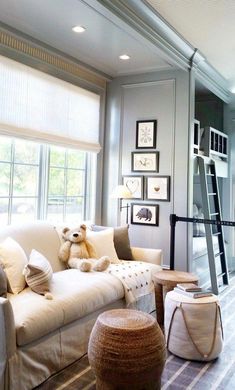 a teddy bear sitting on a couch in a living room next to a window and stairs