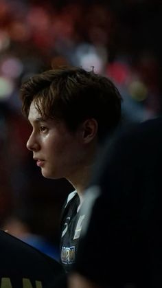 a young man sitting in front of a crowd at a basketball game looking off to the side