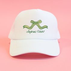 a white cap with green ribbon and the words alpen tau on it against a pink background