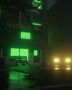 two cars parked in front of a tall building at night with green lights on the windows