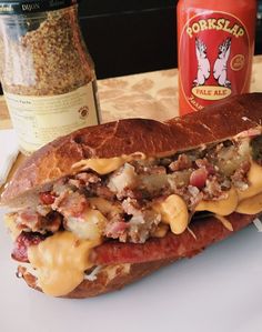 a sandwich with cheese and meat on it sitting on a plate next to a bottle of mustard