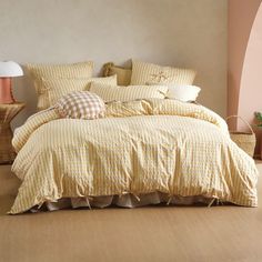 a bed with yellow comforter and pillows in a room next to a lamp on the floor