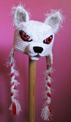 a crocheted white bear hat with red eyes on a wooden stick in front of a pink wall