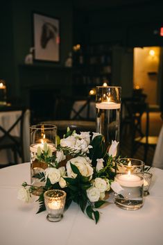 white flowers and candles on a table in a room with other tables set up for an event