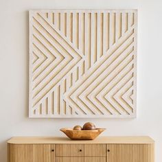 a wooden bowl sitting on top of a dresser next to a wall mounted art piece