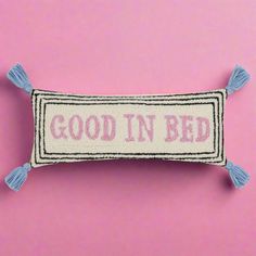 a pillow with the words good in bed on it and tassels hanging down