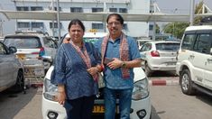 two people standing next to each other in front of a white car with cars behind them