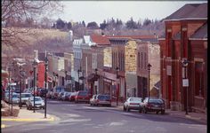 cars are parked on the street in front of buildings and trees, along with other small businesses