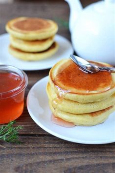 pancakes on white plates with syrup and tea in the background, sitting on a wooden table