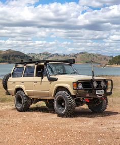 an off - road vehicle parked on the side of a dirt road next to a body of water