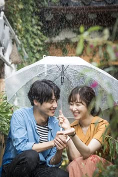 a man and woman sitting under an umbrella in the rain, smiling at each other