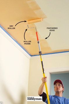 a man is painting the ceiling with paint rollers and a yellow pole in front of him