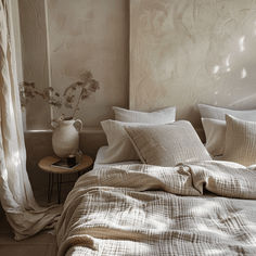 a bed sitting next to a window covered in white sheets and pillows on top of a wooden table