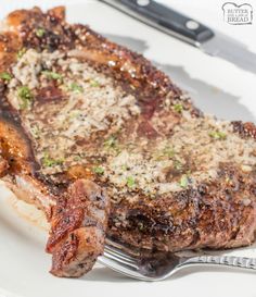 a piece of steak on a white plate with a fork and knife next to it