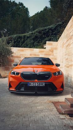 an orange sports car parked in front of a brick wall and steps with trees behind it