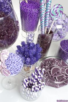 purple and white candies in glass vases next to other candy items on a table