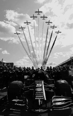 black and white photograph of an air show with jets in the sky over a race car