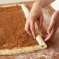 a person kneading dough on top of a wooden table with a rolling pin