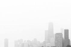 a black and white photo of a city skyline in the fog with sheep grazing on grass