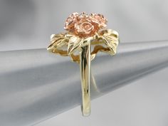 This pretty ring was crafted by the mid-century, with 14 karat gold in leaves and roses of rose gold forming a sweet bouquet center. This pretty piece has a stunning round brilliant diamond, a sparkling contrast to the softly textured petals of the flower.Metal: 14K Yellow and Rose GoldGem: Diamond .11 Carats, SI1 in Clarity, G in ColorGem Measurements: 3.0 mm, RoundRing Size: 4.75 Rose Gold Flower Ring With Prong Setting For Anniversary, Rose Flower Ring For Anniversary, Fine Jewelry, Rose-colored Fine Jewelry Flower Ring For Anniversary, Rose Flower 14k Gold Anniversary Ring, Heirloom Rose Gold Flower Ring, Formal Rose Flower Shaped Rings, Formal Rose Flower Rings, Formal Rose Colored Flower Shaped Rings, Formal Flower Shaped Rings With Rose Design