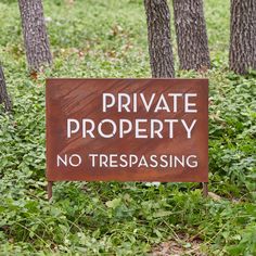 a private property sign sitting in the middle of some grass with trees behind it and no trespassing