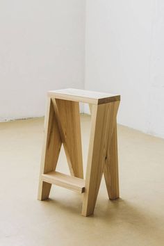 a small wooden stool sitting on top of a floor next to a white wall in an empty room