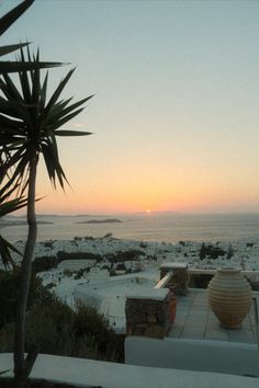 the sun is setting over the beach and ocean from an outdoor patio area with benches