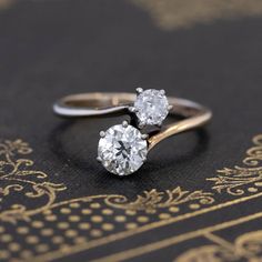 two diamond engagement rings sitting on top of a black book with gold trimmings