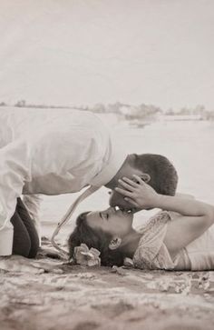 a man kissing a woman on the beach with his head in her hands, while she kisses him