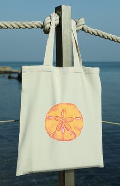 "This Sand Dollar Cotton Canvas Tote Bag is the perfect blend of coastal charm and bright sunshine colors. Whether you're heading to the beach, strolling through a farmer's market, or simply running errands around town, this tote bag is your ideal companion. 🐚 Design: The Sand Dollar Tote Bag features a bright print of a watercolor painting that evokes the shine of a sunny day at the beach. The sand dollar will remind you of peaceful days with your toes in the sand. The print is on one side of Natural Cotton Canvas Beach Bag, Beige Cotton Beach Bag For Beach Season, Natural Cotton Beach Bag For Beach Season, Natural Canvas Bag For Summer Gift, Natural Cotton Beach Bag For Summer, Summer Style Cotton Canvas Bag For Gift, Casual Beach Bag For Gift, Cotton Beach Bag For Beach Season, Rectangular Cotton Beach Bag