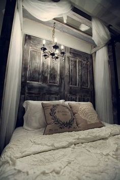 a bed with white sheets and pillows under a wooden headboard that has curtains over it