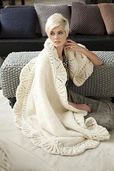 a woman is sitting on a couch with a blanket over her head and wearing a sweater