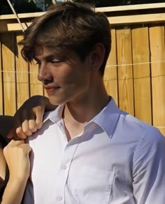 a young man and woman standing next to each other in front of a wooden fence