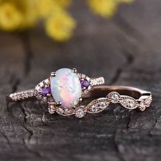 an opal and diamond ring set on top of a piece of wood with flowers in the background