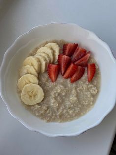 a bowl of oatmeal with sliced bananas and strawberries in it on a table